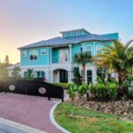 The Hemingway two story home with entrance gate, shown at sunset with large palm trees in front of property